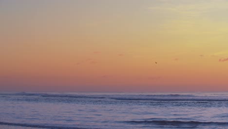Bright-color-sky-after-sunset-over-ocean-waves-in-slow-motion-shot