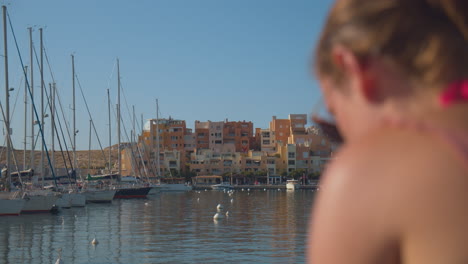 Frau-Sitzt-Am-Ufer-Mit-Segelbooten-Angedockt-Am-Jachthafen-Auf-Der-Insel-Frioul-In-Marseille,-Frankreich