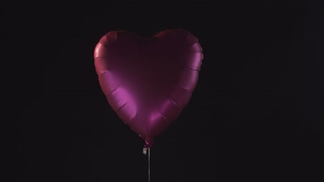 Ein-Einsamer-Pinkfarbener-Herzballon,-Der-Langsam-Auf-Einem-Dunklen-Hintergrund-Schwebt-Und-Sich-Dreht