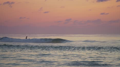 Ein-Einsamer-Surfer,-Der-Einen-Kühlen,-Farbenfrohen-Sonnenuntergang-Mit-Rollenden-Wellen-Beobachtet