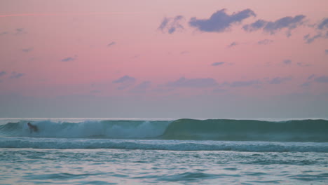 A-surfer-catching-a-wave-with-a-beautiful-pink-and-blue-sunset-behind-him
