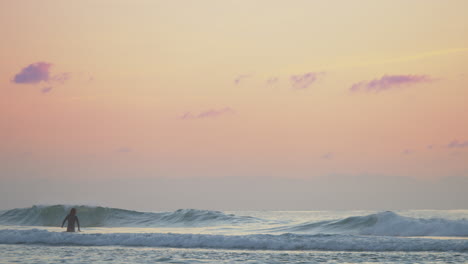 Ein-Wunderschöner-Nebliger-Orangefarbener-Sonnenuntergang-Mit-Einem-Einsamen-Surfer,-Der-Die-Wellen-Fängt