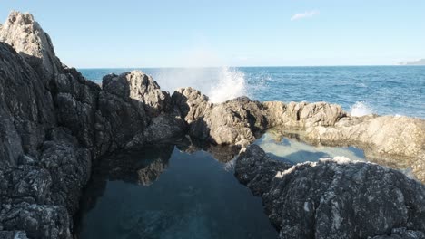 Huge-ocean-splash-falls-over-tall-jagged-rock-into-natural-pool