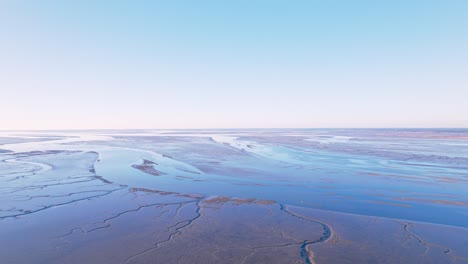 Drohnenansicht-Der-Meeresküste-Bei-Ebbe-Sandformation-Und-Wunderschöner-Spiegelung-Des-Blauen-Himmels