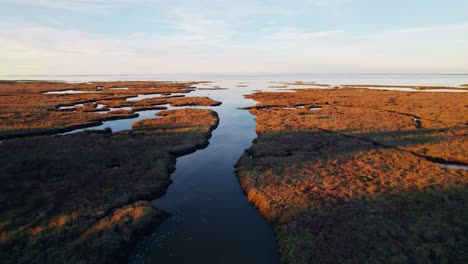 Small-river-leading-to-massive-lake-surrounded-by-wetlands,-aerial-drone-shot