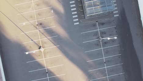 Empty-parking-lot-with-white-lines-and-light-poles,-aerial-top-down-shot