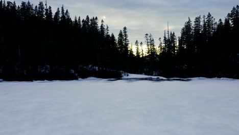 Ascending-drone-dolly-shot-over-a-frozen-lake-and-trees-towards-a-bright-sunny-sky