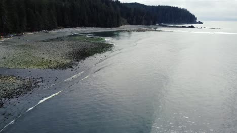 Drohnenaufnahme-über-Einem-Sandigen-Und-Felsigen-Strand-Mit-Wald-Im-Hintergrund