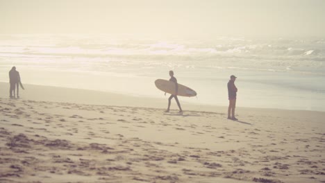 Surfer-holding-surfboard-and-walking-away-from-ocean-water-and-waves-on-sunny-dusk-time