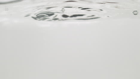 Water-drops-falling-on-calm-surface-isolated-on-pure-white-color,-close-up