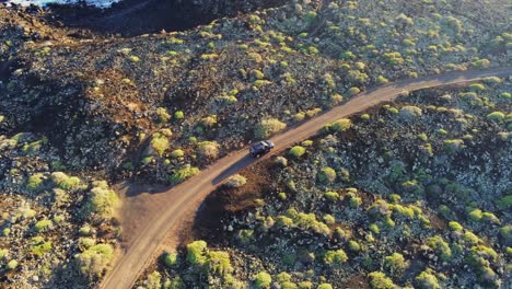 Vehículo-Negro-Conduciendo-Por-Una-Carretera-Costera-De-Tierra-En-Terreno-Rocoso-En-La-Isla-De-Lanzarote,-Vista-Aérea