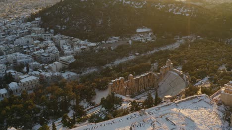 Aerial-view-over-the-snowy-Acropolis-hill,-towards-the-Herodes-atticus-odeon,-sunny-winter-evening-in-Athens---tilt,-drone-shot
