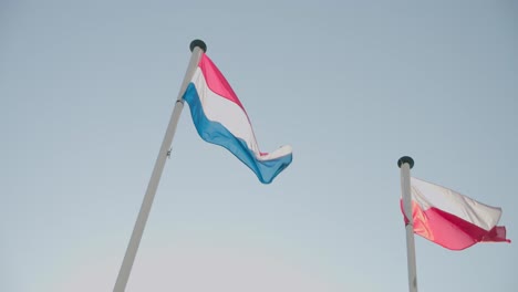 Low-angle-shot-of-Luxembourg-and-Poland-flag-waving-in-wind