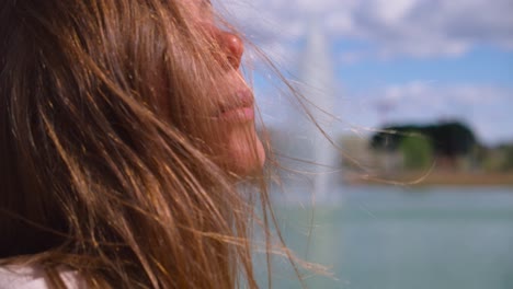 Close-up-of-young-girl-standing-beside-lake-and-enjoying-pleasant-wind-over-her-face-ruffling-through-her-hair