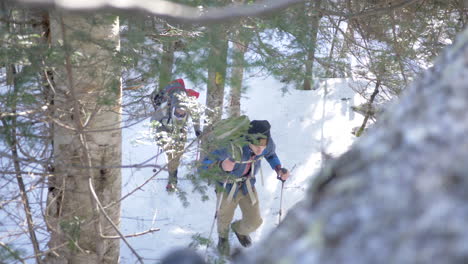 Disparo-En-ángulo-Alto-De-Dos-Hombres-Escalando-Una-Montaña-Nevada-En-Los-Bosques-De-New-Hampshire