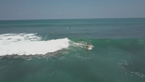Toma-Aérea-De-Una-Mujer-Surfista-Atrapando-Una-Ola-Y-Cabalgando-Durante-Una-Sesión-De-Surf-En-Los-Mares-Azules-De-Costa-Rica