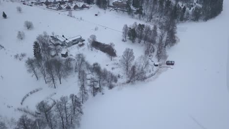 Overhead-shot-of-picturesque-rural-community-dressed-in-a-beautiful-winter-coat-on-the-edge-of-big-frozen-lake