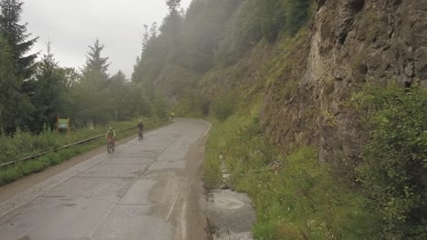 Vista-Aérea-De-Un-Par-De-Ciclistas-Vendiendo-En-Un-Camino-Brumoso-En-Colbita,-Rumania-Durante-La-Carrera-De-Bicicletas-Tura-Cu-Copaci