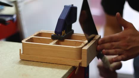 In-a-Workshop,-a-man-uses-a-Japanese-Saw-to-saw-off-some-some-wood-from-a-clamped-down-work-piece