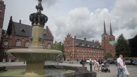 People-walking-by-a-fountain-in-front-of-UNESCO-World-Heritage-church-Roskilde-Cathedral-in-Roskilde,-Denmark