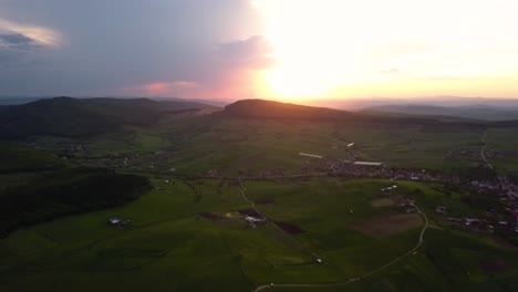 Panorama-aerial-shot-of-a-beautiful-sunset-over-open-country-with-green-meadows-and-fields,-Transylvania,-Romania