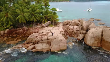 Luftdrohnenaufnahme-Eines-Einsamen,-Aber-Glücklichen-Mannes,-Der-Auf-Einer-Kleinen-Tropischen-Insel-Auf-Den-Seychellen-Steht