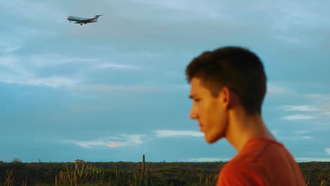In-the-shot-you-can-see-young-man-profile-standing-in-frame-while-huge-airplane-is-landing-in-background