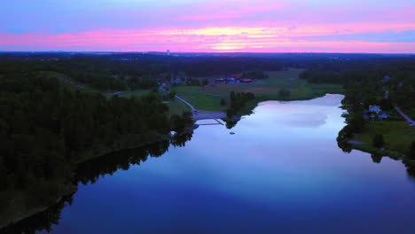 Aerial-drone-view-over-a-lake-and-towards-the-countryside,-a-purple-sky,-at-a-colorful-sunset-or-dusk,-at-Albysjon,-Tyreso,-Sweden