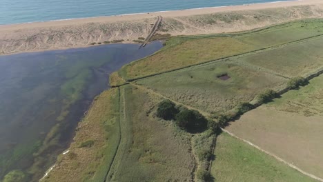 Aerial-tracking-forward-angled-down-on-the-fleet-lagoon-and-the-western-edge-with-mud-tracks-leading-up-to-the-bank-of-Chesil-Beach