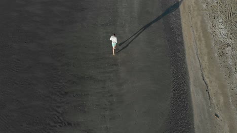 Aerial-tilt-up-shot-of-young-man-running-on-a-beach-in-Auckland,-New-Zealand