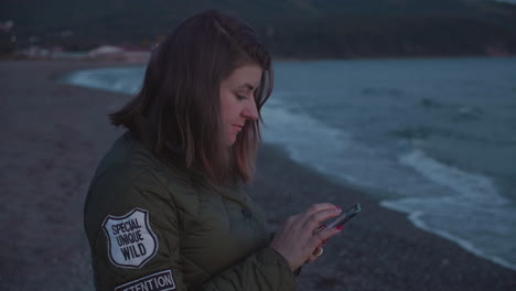 Slow-motion-shot-of-a-girl-using-her-phone-on-the-beach-on-the-sunset