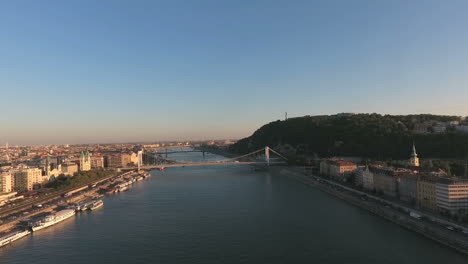 Toma-Aérea-De-Budapest,-Acercándose-A-La-Montaña-Gellert,-Con-La-Estatua-De-La-Libertad,-Mostrando-El-Petofi-Y-El-Puente-Szabadsag