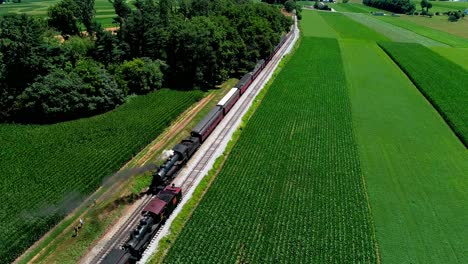 Steam-Train-at-Picnic-Area,-Dropping-off-Passengers-as-Second-Steam-Train-Passes,-in-Amish-Countryside-as-seen-by-Drone