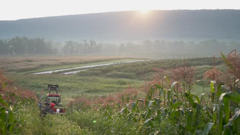 Camera-moving-away-from-a-loaded-tractor-in-the-cornfield-as-the-sun-rises-over-the-mountain-in-the-distance