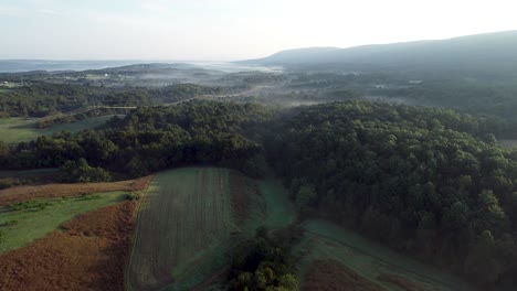 Aerial-camera-ascending-view-of-West-Virginia-countryside-with-farms,-fields,-mountains-and-fog-settling-in-the-valleys