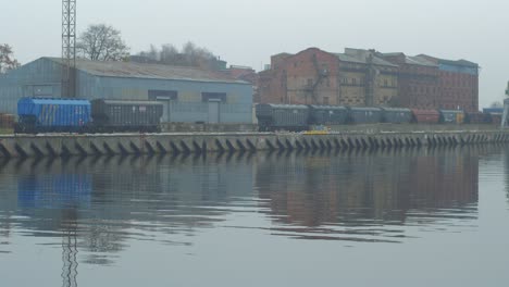 Coal-wagons-parked-at-Port-of-Liepaja,-ready-for-loading-in-foggy-day,-reflections-in-water,-wide-shot