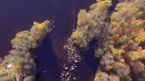 Aerial-footage-of-a-river-with-three-boats-on-land-and-autumn-colored-forest-surroundings