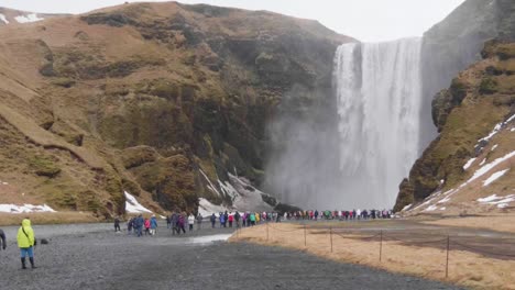 Static,-slow-motion-shot-of-lots-of-people-enjoying-the-view-of-Skogafoss-waterfall,-on-a-cloudy,-autumn-day,-in-Iceland