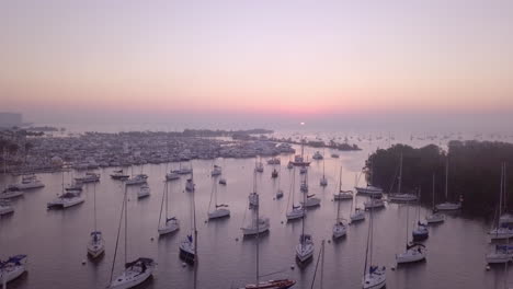 Aerial-high-angle-fly-over-boat-filled-harbor-towards-pink-sunrise