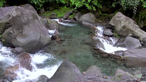 Kleine-Wasserfälle,-Die-In-Ein-Flaches-Becken-Mit-Klarem,-Erfrischendem-Bergwasser-Mit-Felsbrocken-Und-Felsen-In-Einem-Dschungelregenwald-Ein--Und-Ausströmen