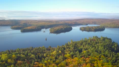 Aerial-Daytime-Wide-Shot-Of-Calm-Lake-With-Boat-And-Pine-Tree-Islands-And-Reflections-Descending-Towards-Fall-Forest-Colors-In-Kawarthas-Ontario-Canada