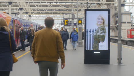 Digitales-Vertikales-Werbedisplay-An-Einem-Großen-Bahnhof-Mit-Fahrgästen,-Die-In-Einen-Zug-Einsteigen