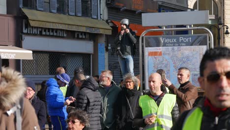 Ein-Fotojournalist-Setzt-Seinen-Helm-Auf,-Während-Er-Neben-Einer-U-bahnstation-In-Marseille,-Südfrankreich,-Eine-Menge-Von-Demonstranten-In-Gelben-Jacken-Beobachtet