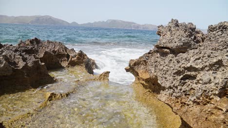 Winzige-Wellen,-Die-Auf-Felsen-Auf-Mallorca-Baleareninsel-Spanien,-Umgeben-Von-Bergen,-Zusammenstoßen