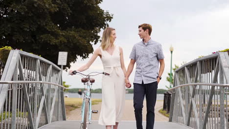 Young-couple-holding-hands-and-walking-over-a-bridge-in-a-park