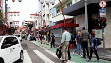 Escena-Panorámica-Desde-La-Esquina-De-La-Calle-Hasta-Una-Vista-De-La-Entrada-Del-Barrio-Japonés-De-Liberdade-En-São-Paulo,-Brasil,-Con-Decoración-Típica-En-La-Principal-Calle-Comercial