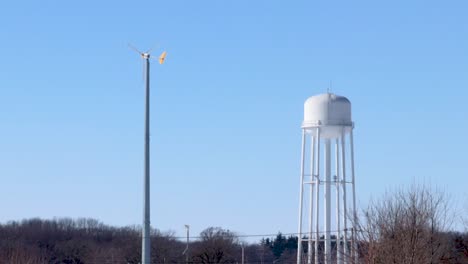 A-still-shot-of-a-small-wind-turbine-and-a-water-tower-during-a-windy-cloudless-afternoon
