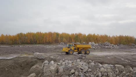 Drohnenaufnahme-Aus-Der-Luft,-Die-Einem-Sattelschlepper-Hinterherfährt,-Der-Auf-Einen-Raupenbagger,-Volvo-Ec380el,-Zufährt-Und-An-Einer-Sandgrube-In-Pohjanmaa,-Finnland,-Gräbt