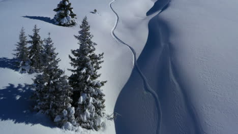 Aerial-view-following-up-a-snowy-gully-following-a-snowboard-track-in-fresh-powder