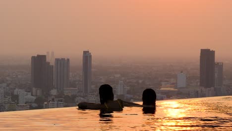 Girls-chilling-in-a-infinity-pool-at-sunset-in-a-big-city,-Bangkok,-Thailand
